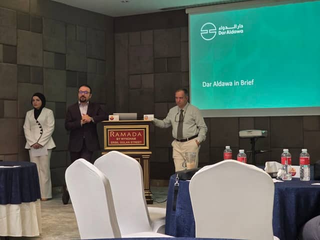 Dr. Karzan standing by the lectern with two colleagues, a Dar Aldawa slide on the screen