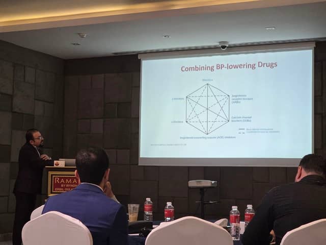Dr. Karzan at the lectern beside a slide titled Combining BP-lowering Drugs