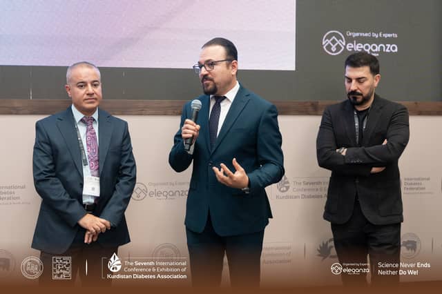 Dr. Karzan speaking into a microphone between two colleagues